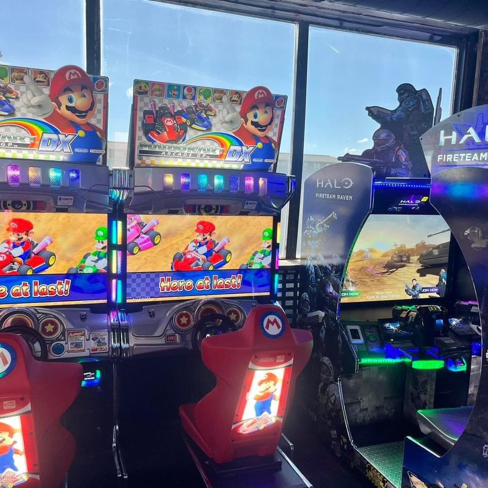 Two Mario Kart cabinets and a Halo cabinet beside sunny second-floor windows.
