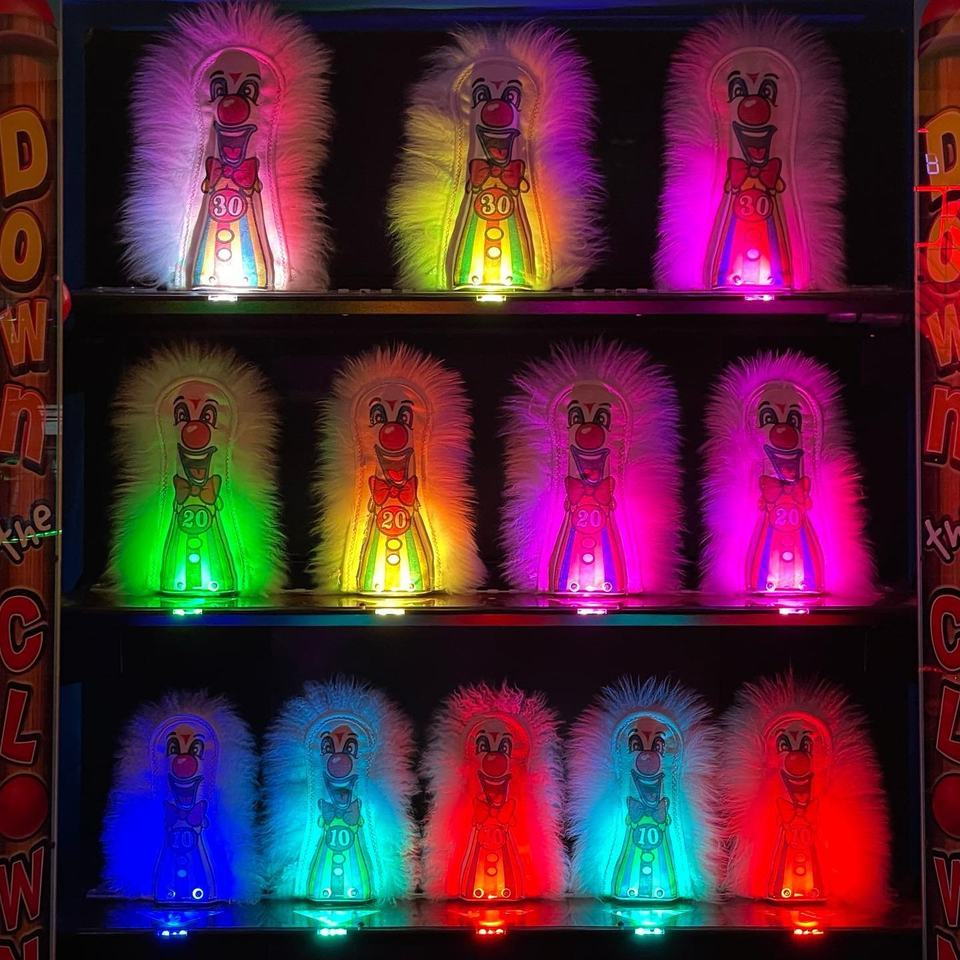 A wall of glowing clown targets in pink, yellow, green and blue on a carnival arcade game.