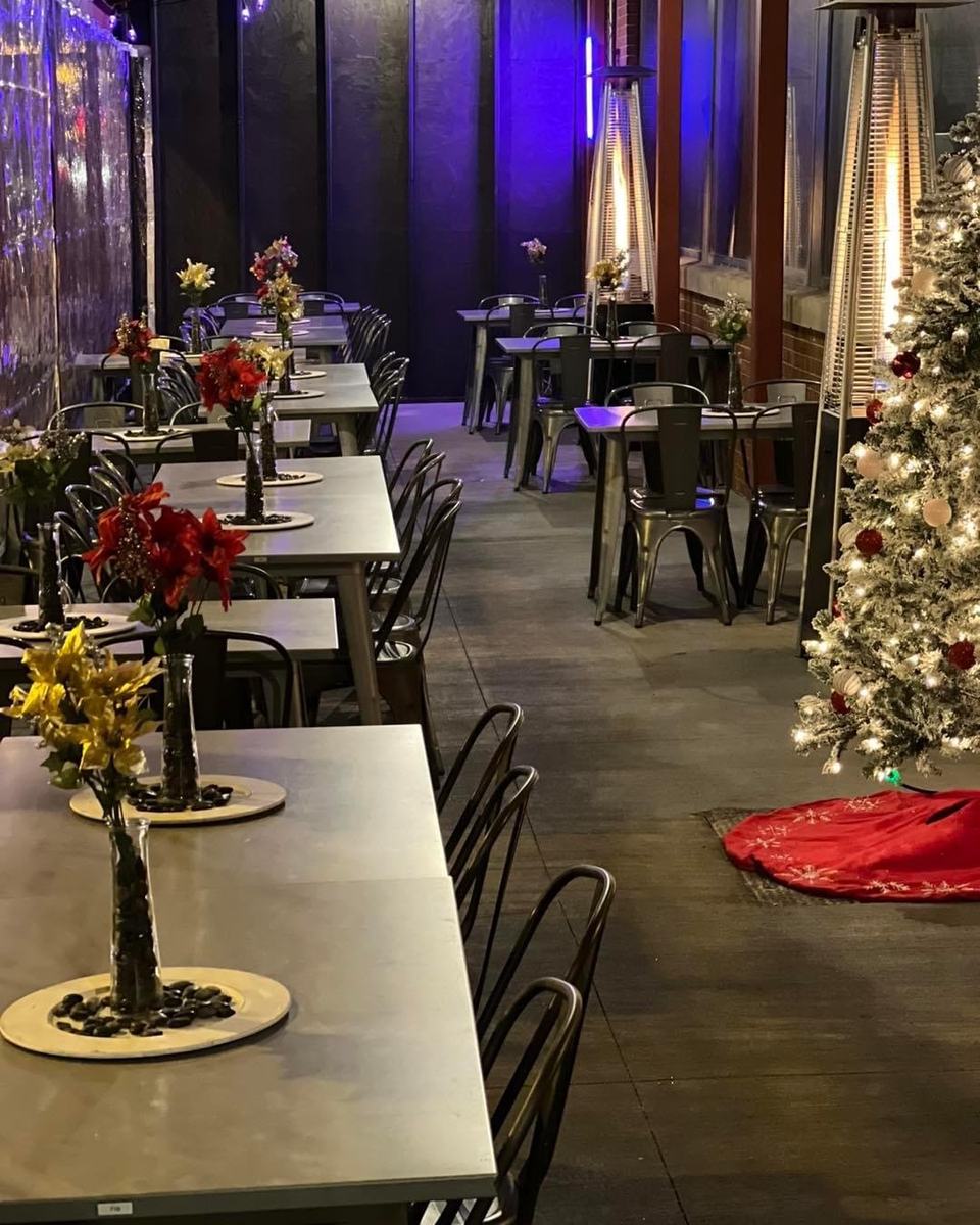 The event room set with long tables, flower centerpieces, tall patio heaters and a decorated tree.