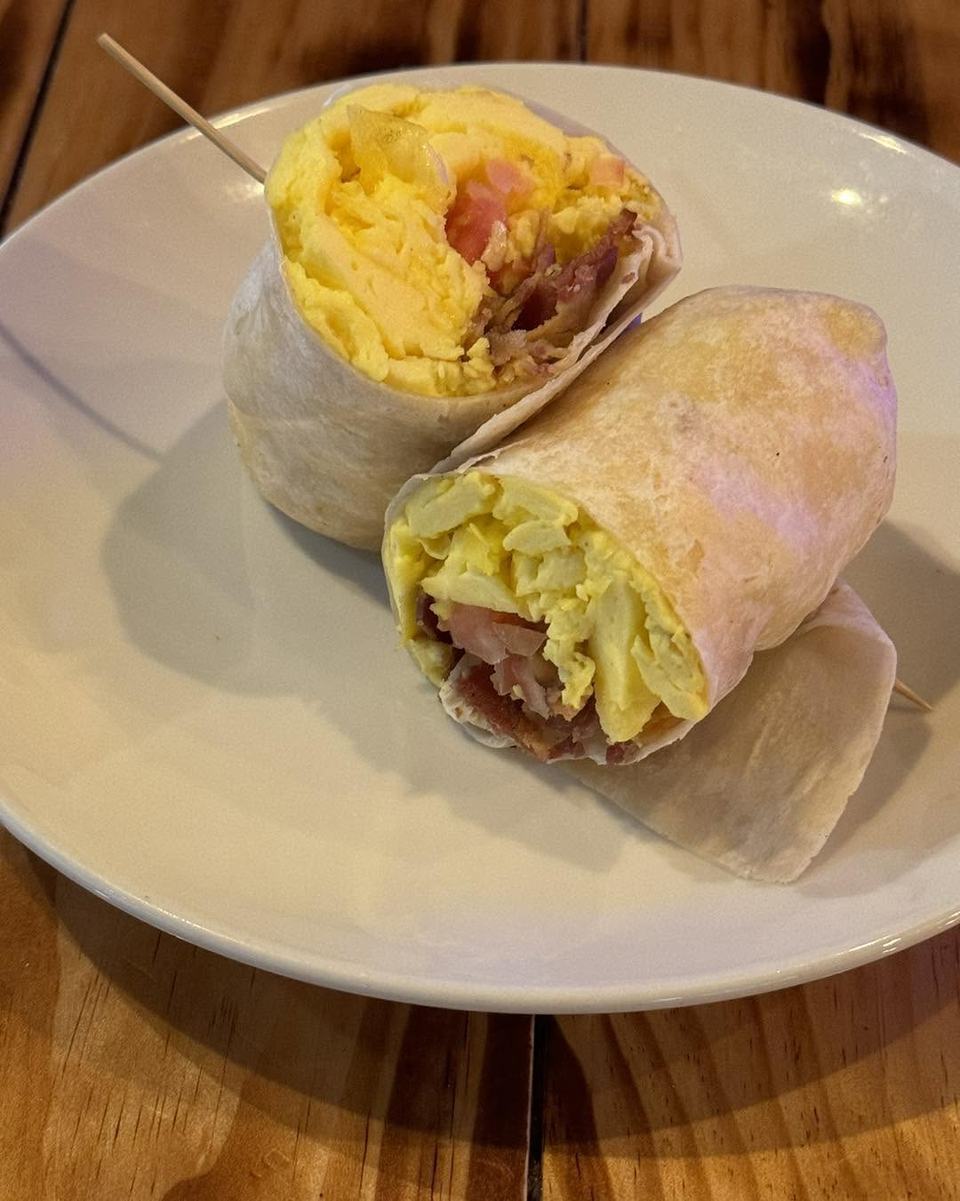 Two halves of a breakfast burrito showing scrambled egg and bacon, on a white plate.