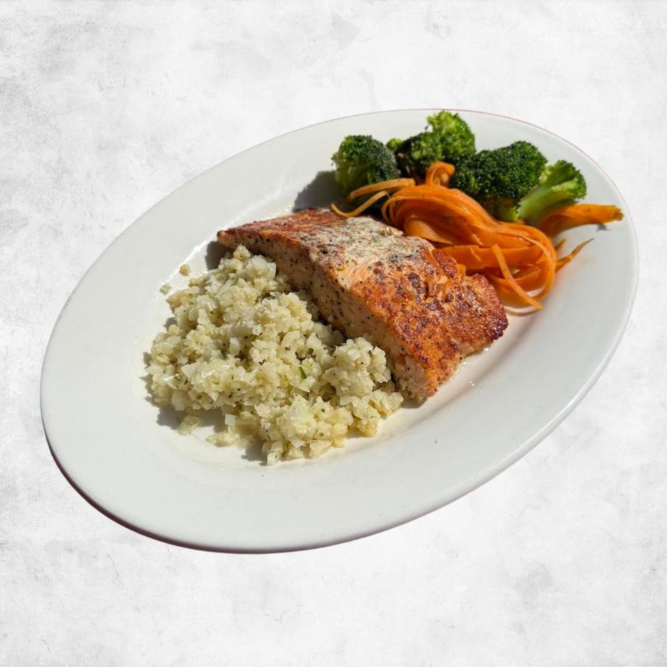 A seared salmon fillet on riced cauliflower with broccoli and shredded carrot, on a white oval plate.