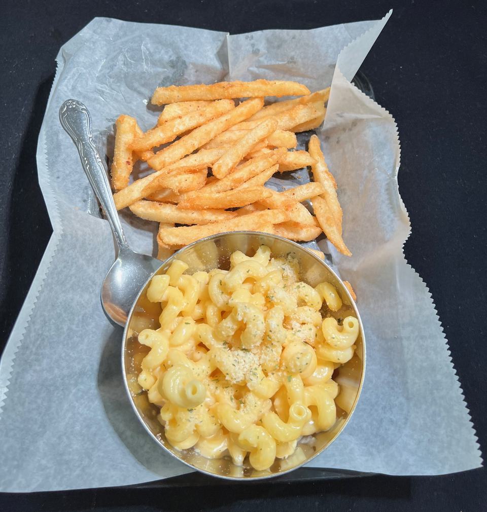 Kids' mac and cheese in a steel cup with a spoon, beside a basket of fries.