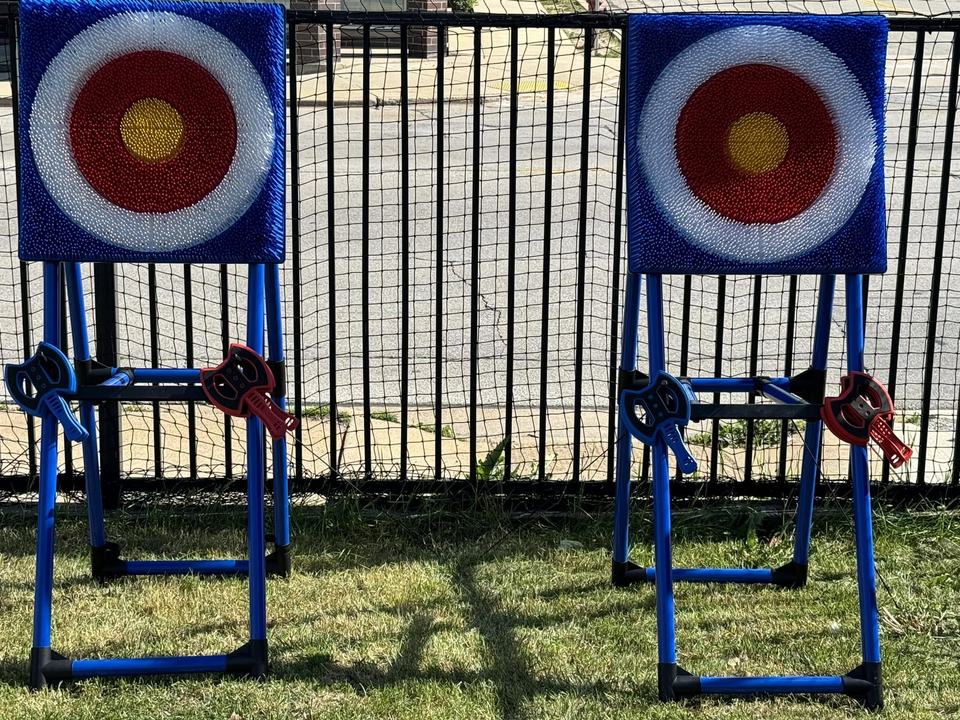 Two bullseye target stands with throwing axes leaning on their frames, against the black fence.