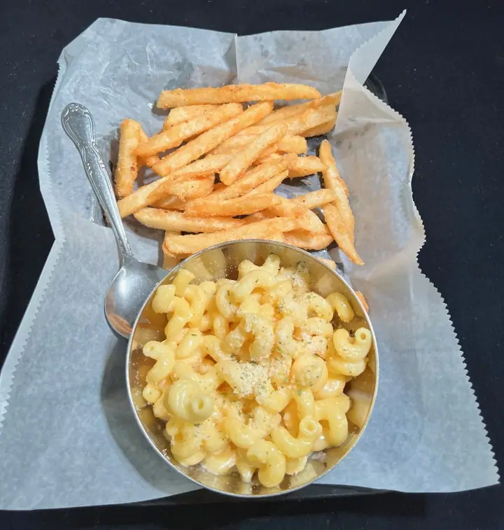 I Don't Care: macaroni and cheese in a steel cup with a spoon, beside a basket of fries.