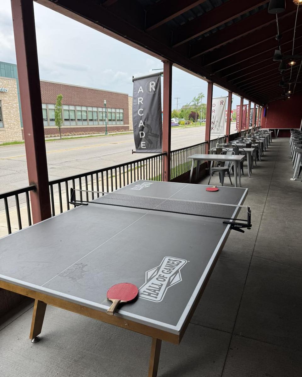 The covered patio in daylight with a ping pong table in the foreground and tables down the walkway, no guests.