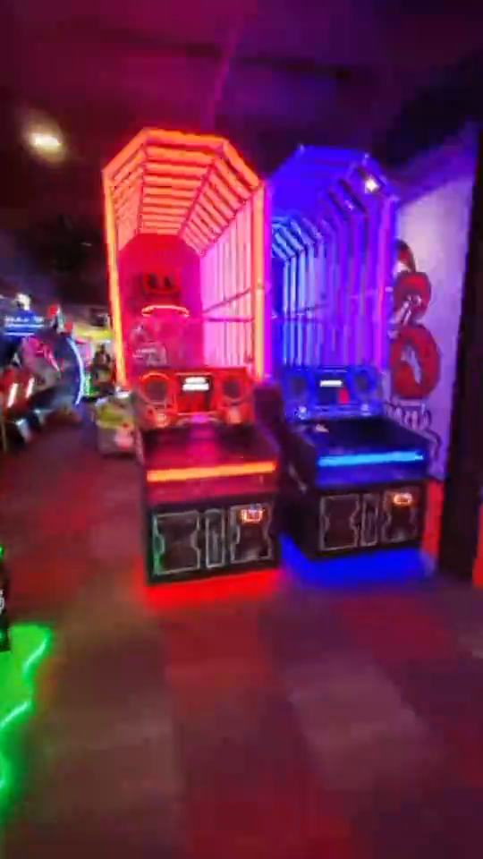 A pass through the arcade: glowing neon basketball hoops, a ticket game firing a lit ball, racing and shooting cabinets by the windows, then a neon skee-ball lane.