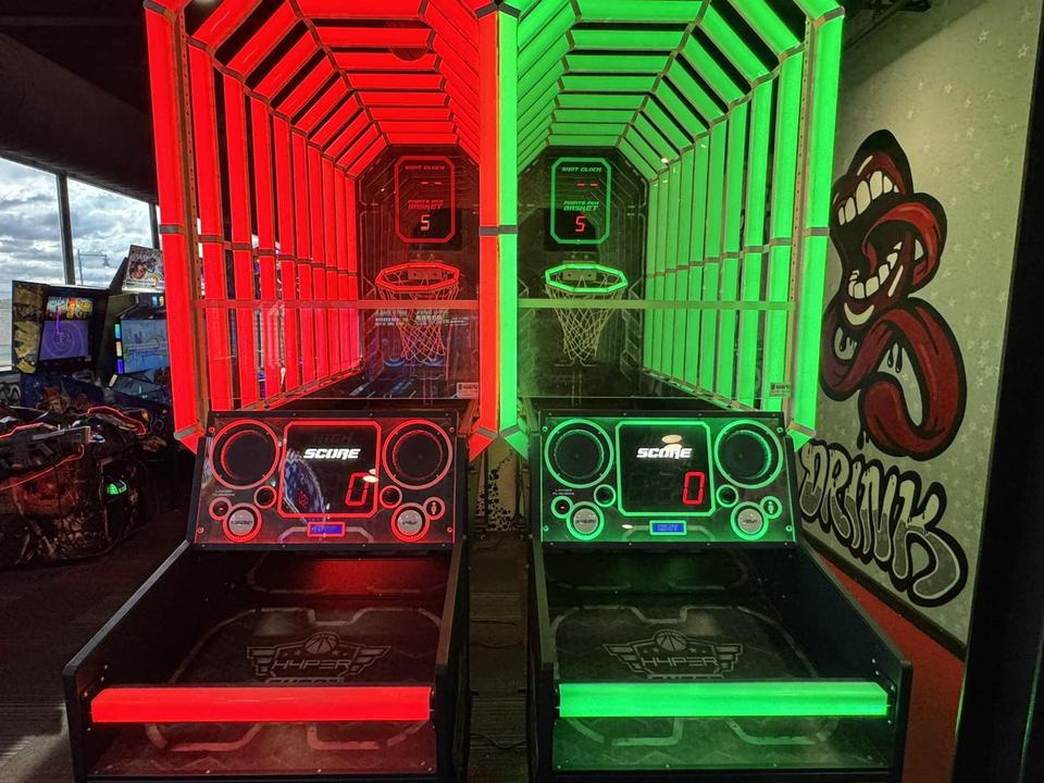 A red-lipped open mouth with a tongue running into wildstyle DRINK lettering on the white star wall beside the red and green basketball cabinets.